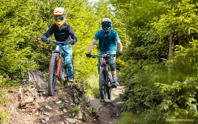 Ein Vater fährt mit seinem Kind einen Bikepark Trail runter